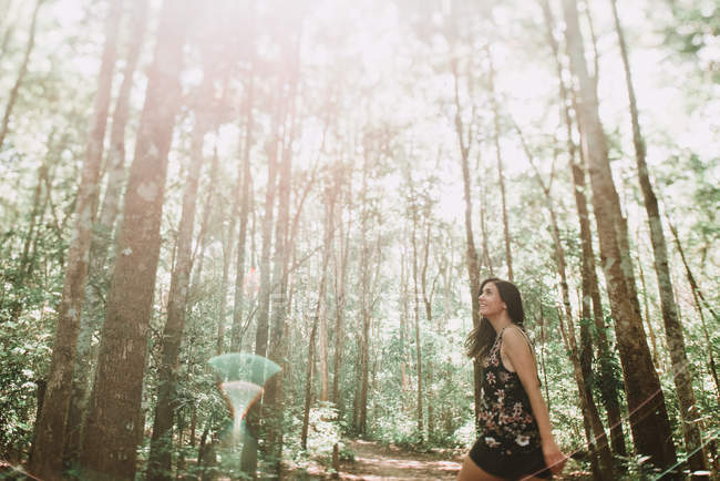 Усміхнена молода жінка, що йде в лісі в сонячний день . — стокове фото