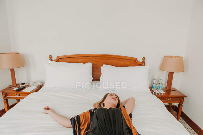 Mujer joven acostada y relajada en la cama en la habitación de hotel - foto de stock