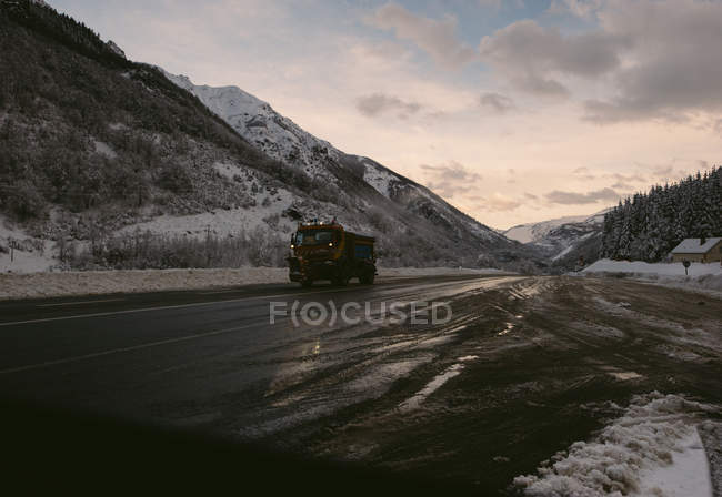 Промышленный грузовик едет по асфальтированной дороге в снежных холмах в зимний день . — стоковое фото