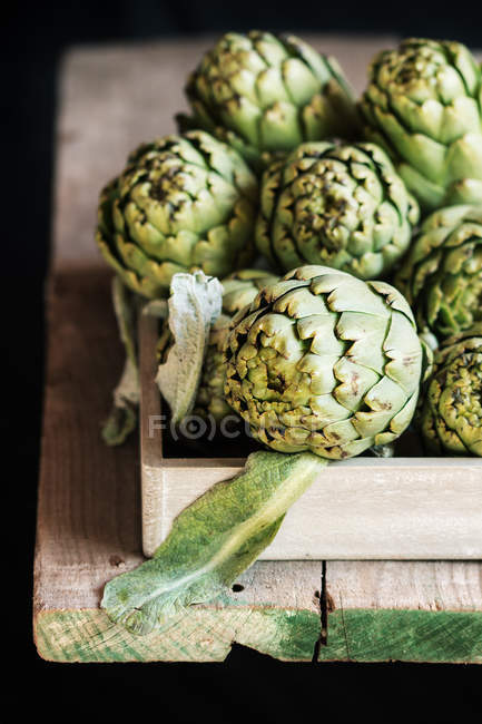 Raw artichokes in wooden crate on table — Stock Photo
