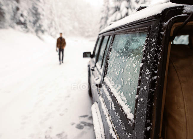 Неузнаваемый турист, идущий к машине, припаркованной на снежной дороге — стоковое фото