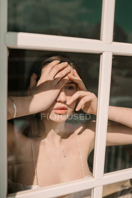 Жінка в бюстгальтері стоїть біля вікна і торкається обличчя в сонячний день . — стокове фото