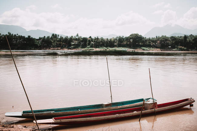 Barche lunghe a riva con acqua sporca in giornata nuvolosa . — Foto stock