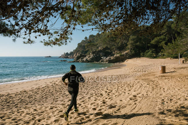 Vue arrière de l'homme faisant du jogging à la plage de sable — Photo de stock