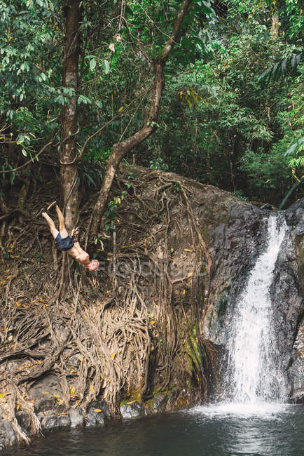 Человек без рубашки висит на дереве над прудом в джунглях — стоковое фото