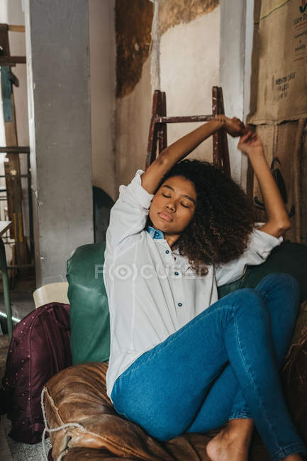 Hübsche junge ethnische Frau sitzt auf dem Sofa und streckt die Hände aus — Stockfoto