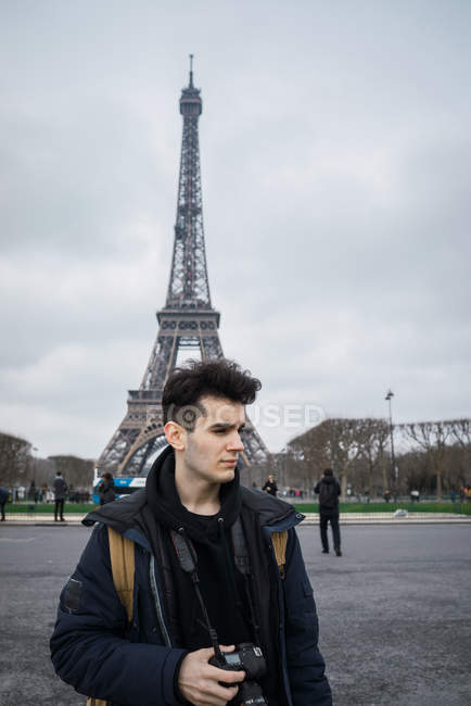 Молодий туристичних людина з камерою стоячи над Ейфелевої вежі і дивитися вбік — стокове фото
