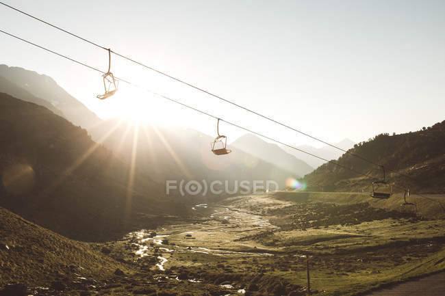 Picturesque view to ropeway moving over green mountains in sunset lights. — Stock Photo
