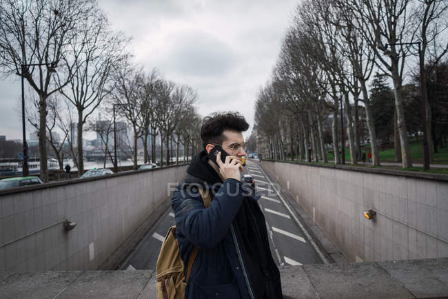Young man standing and talking on smartphone at street — Stock Photo