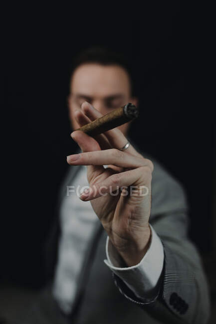 Primer plano mano de hombre guapo en traje fumar cigarro sobre fondo oscuro. - foto de stock