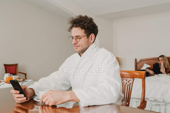 Hombre en albornoz de navegación smartphone en la habitación del hotel - foto de stock