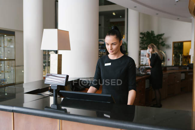 Joven trabajador de hotel morena trabajando en recepción - foto de stock