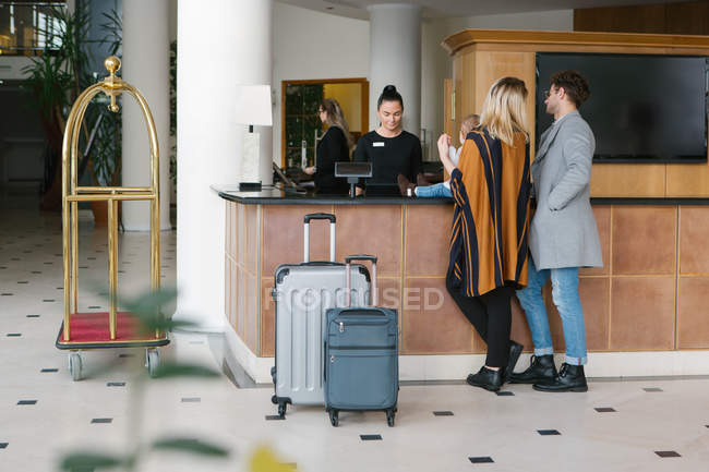 Rear view of young family at reception in hotel lobby — Stock Photo