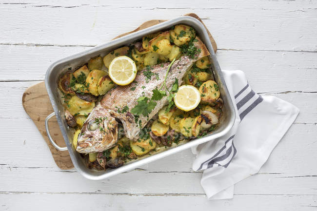 Roasted fish with potatoes and salad on wooden table — Stock Photo