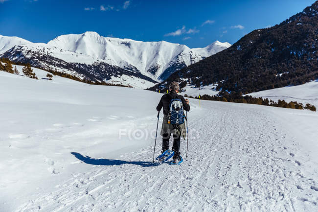 Vista trasera del hombre caminando a través del prado de nieve iluminado por el sol - foto de stock
