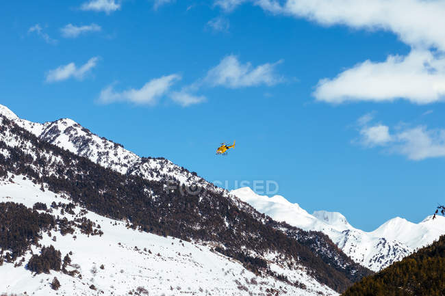 Rescue helicopter flying in mountains over bright sky — Stock Photo