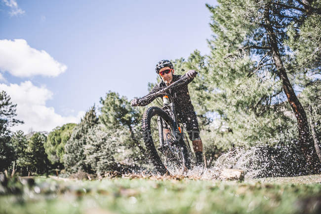 Vista frontal do homem ciclista espirra água com bicicleta de montanha no gramado — Fotografia de Stock