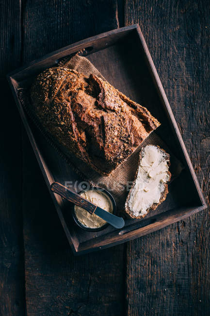 Pão rústico com manteiga na bandeja de madeira rural — Fotografia de Stock