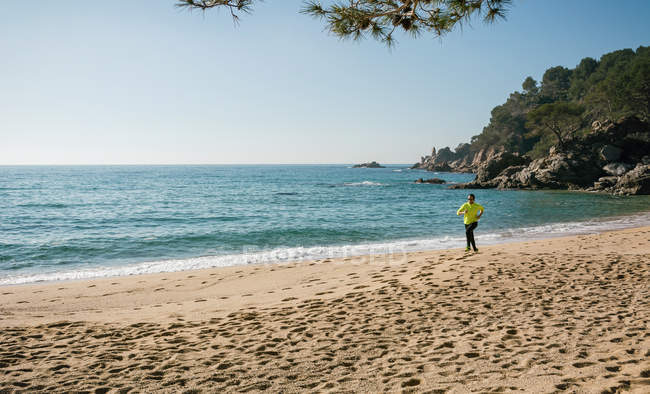 Homme faisant du jogging le long de la mer sur la plage de sable par une journée ensoleillée — Photo de stock