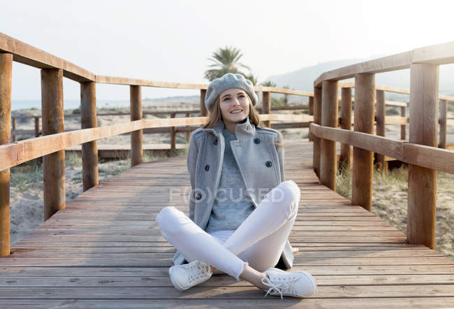 Sorrindo jovem mulher em roupas elegantes sentado no calçadão em dia ensolarado . — Fotografia de Stock