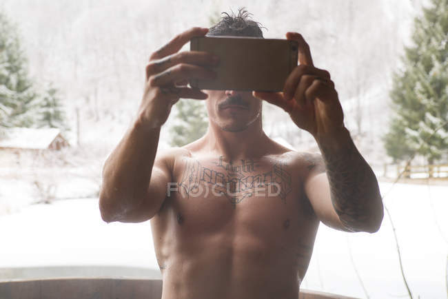Uomo in topless in piedi in vasca immersione e scattare selfie sullo sfondo della natura invernale . — Foto stock