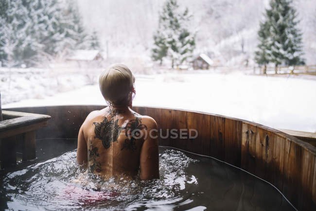 Visão traseira da mulher em pé na banheira de mergulho ao ar livre na natureza de inverno . — Fotografia de Stock