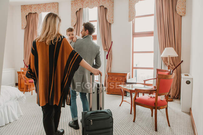 Vista posteriore della famiglia con valigie che camminano in camera d'albergo — Foto stock