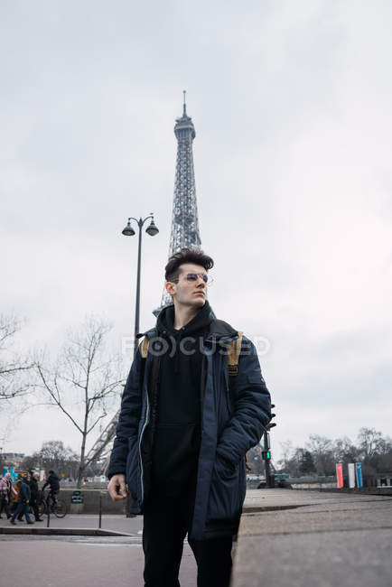 Young man in glasses posing on background of Eiffel tower. — Stock Photo