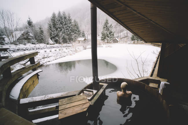 Vista trasera de la mujer nadando en bañera de inmersión al aire libre en el día de invierno - foto de stock