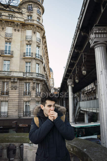 Pensive young heating hands with breath and looking away at street scene — Stock Photo
