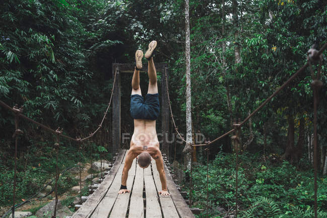 Vue arrière de l'homme torse nu debout sur les mains sur un pont en bois grogneux — Photo de stock