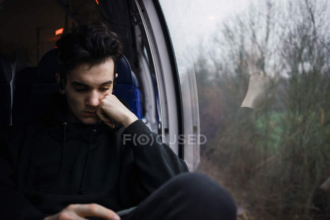 Молодий чоловік сидить і використовує смартфон в автобусі в дощовий день . — стокове фото