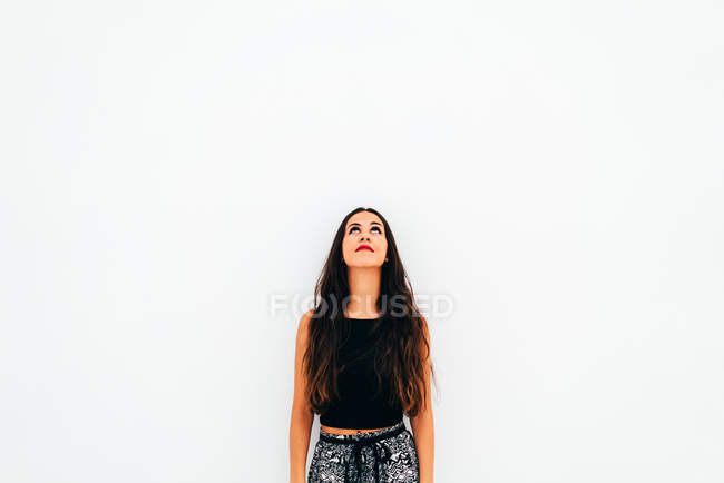 Молодая женщина опирается на белую стену и смотрит вверх — стоковое фото