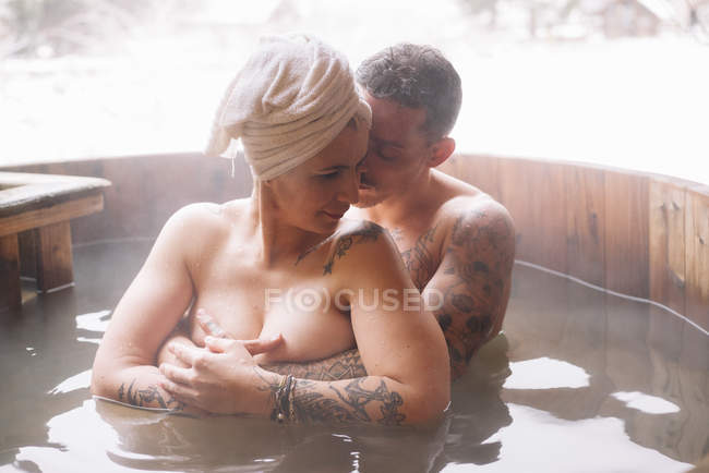 Sensual tattooed couple embracing in outdoor plunge tub in winter. — Stock Photo