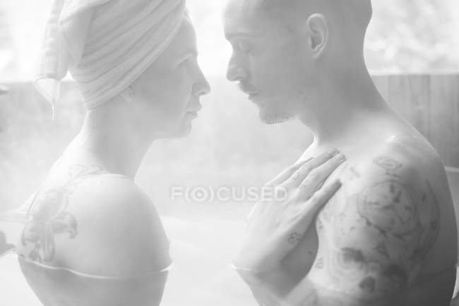 Sensual pareja tatuada sentada y abrazándose en una bañera profunda en invierno . - foto de stock