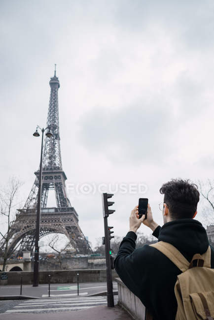 Вид ззаду молодого туриста, який робить знімки Ейфелевої вежі з телефоном — стокове фото