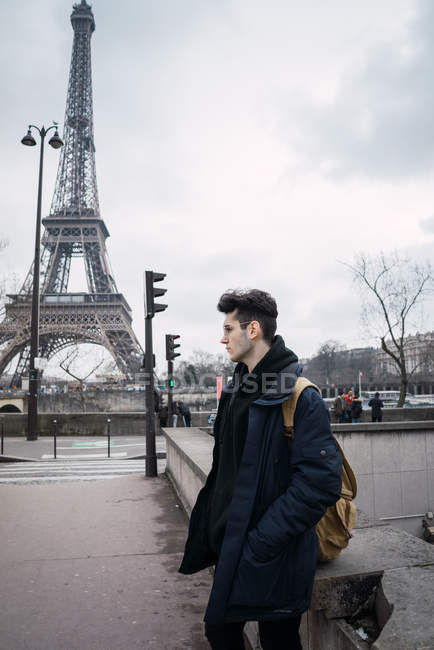 Young man standing on background of Eiffel tower on cloudy day — Stock Photo