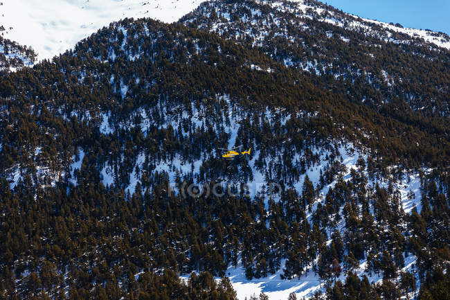 Rescue helicopter flying over tree-covered mountain — Stock Photo