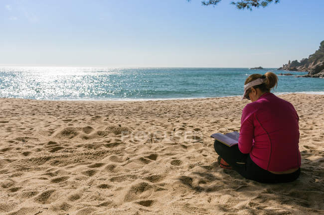 Mujer madura leyendo libro en la playa soleada - foto de stock