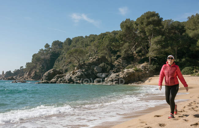 Mujer alegre caminando en la playa y mirando al mar - foto de stock