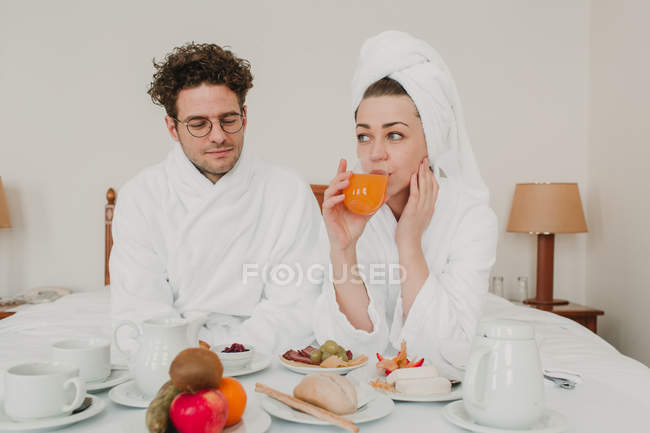 Молода пара снідає в готельному ліжку — стокове фото