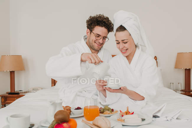 Casal alegre tomando café da manhã na cama do hotel — Fotografia de Stock