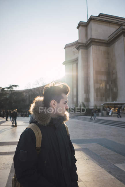 Pensativo joven turista caminando en una gran plaza bajo el sol y mirando hacia otro lado . - foto de stock