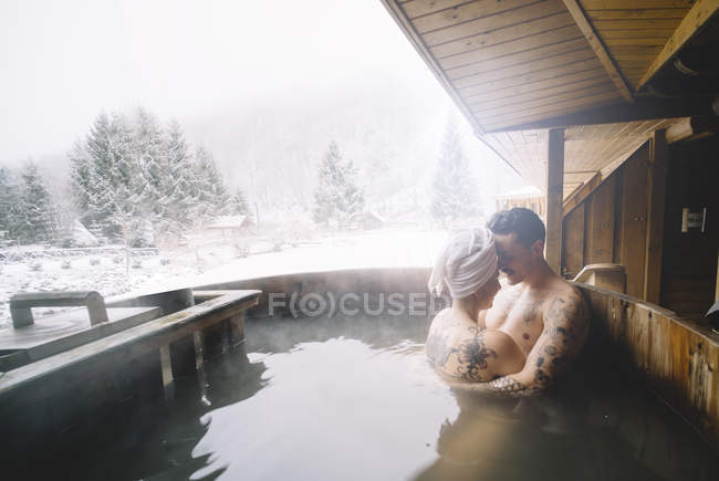 Pareja abrazándose en bañera de inmersión al aire libre en el día de invierno - foto de stock