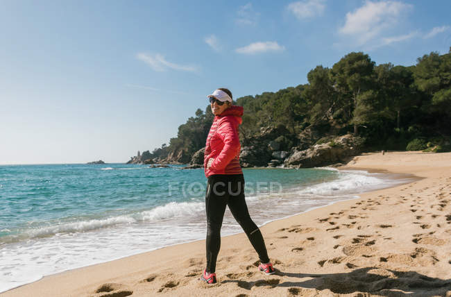 Mulher madura olhando sobre o ombro na câmera na praia — Fotografia de Stock