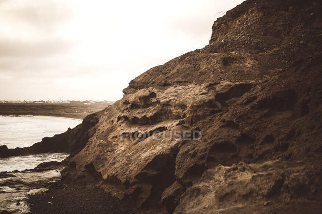 Вид на темну прибережну скелю на березі океану хмарний день . — стокове фото