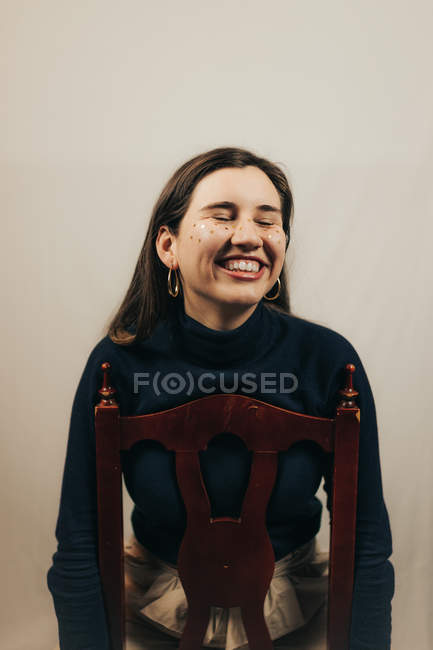 Femme souriante avec des paillettes sur le visage assis sur la chaise — Photo de stock