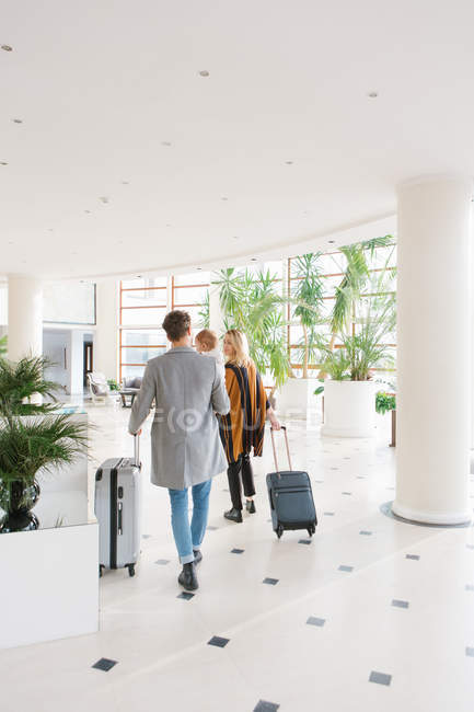 Rear view of family walking with suitcases in hotel hall — Stock Photo