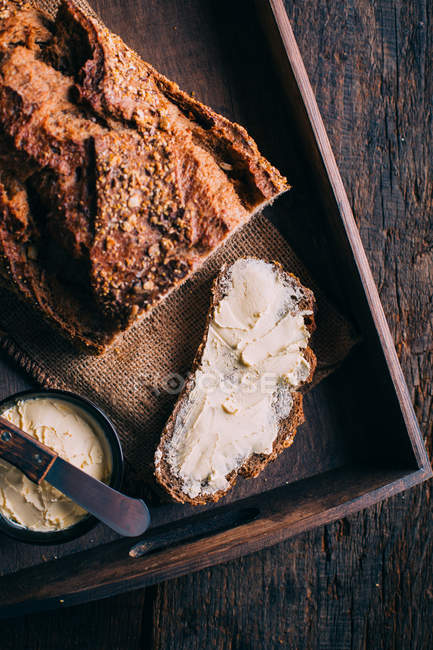 Vue de dessus de tranche de pain rustique avec du beurre sur le plateau — Photo de stock