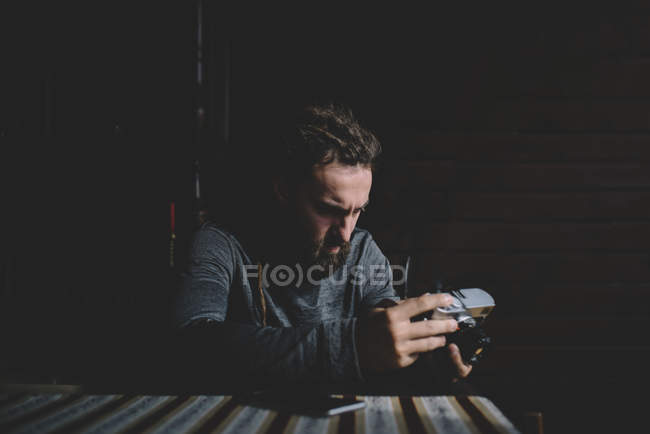 Fotógrafo sentado à mesa e focado com câmera vintage — Fotografia de Stock